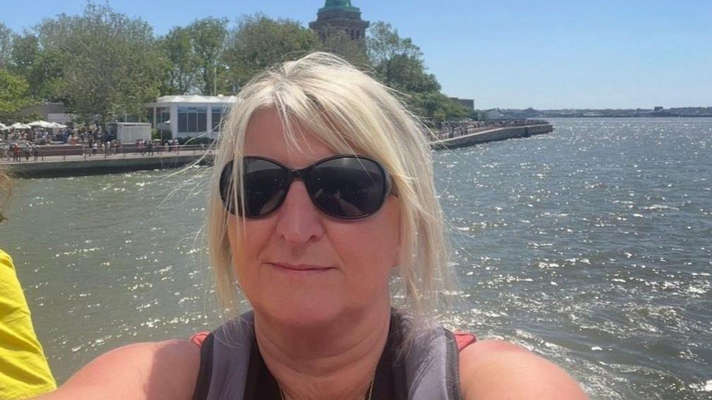 Eve Craven wearing sunglasses looking into the camera with sun shining on the water in the background