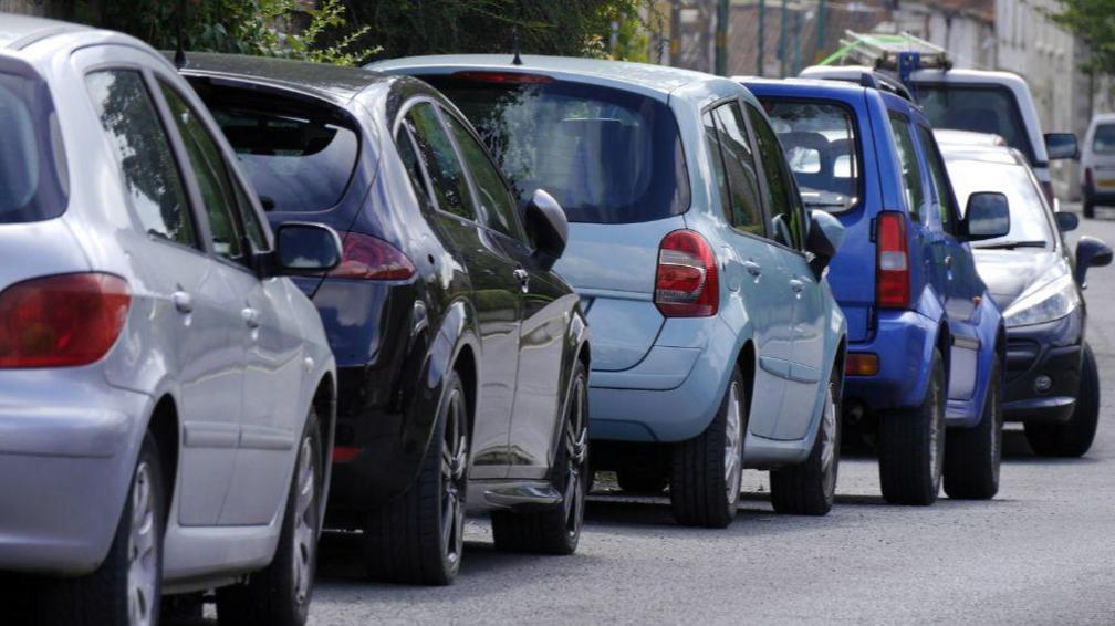 A line of cars parallel parked on the edge of a street.