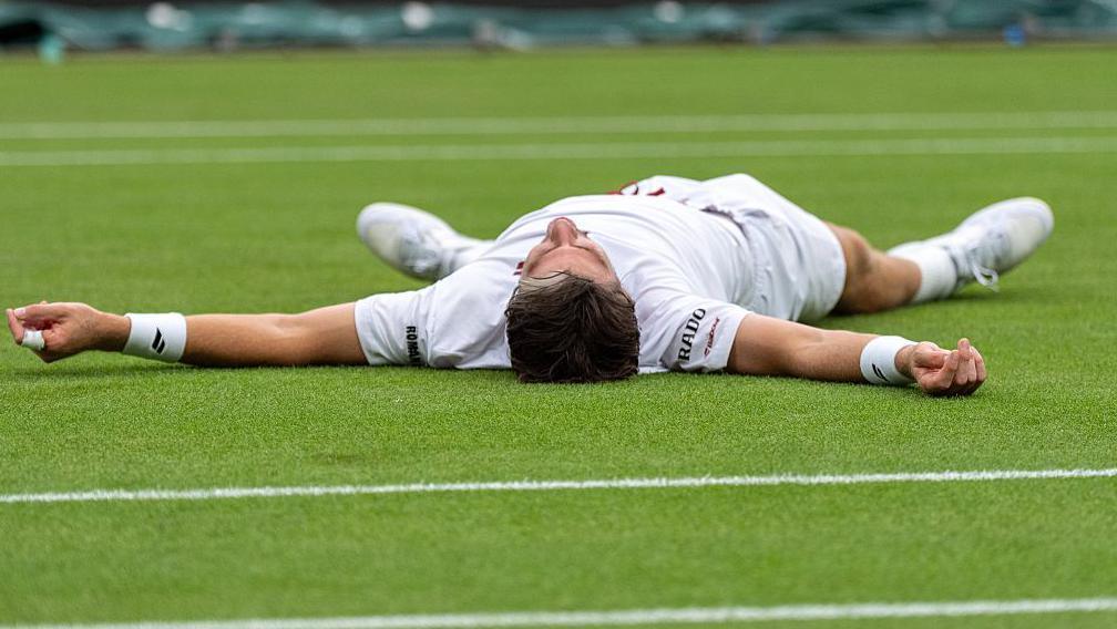 Cameron Norrie celebrates by falling on to the court 