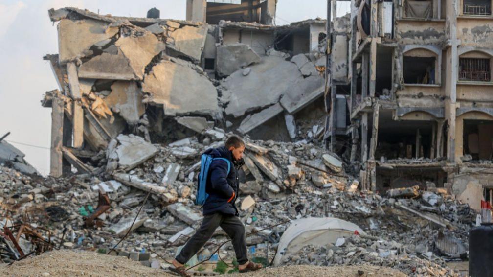 Boy walking past damaged buildings in Khan Yunis, Gaza on 11 January 2025. 