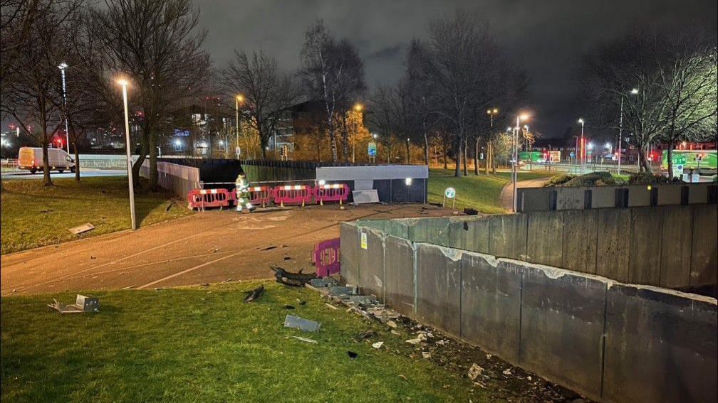 A person in hi-vis clothing walks past pink barriers that have been erected near the point where the car crashed through a wall and plunged down on to the railway line below.