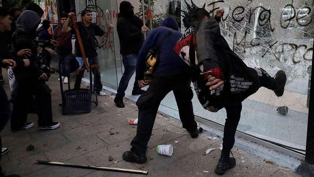 Rioters smashing the windows of an upmarket shop in the Roma district of Mexico City