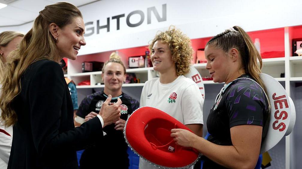 Catherine, Princess of Wales, speaks with Megan Jones, Ellie Kildunne and Jessica Breach in the dressing room as they present her with a red cowboy hat