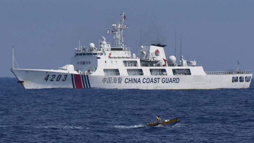 A China Coast Guard ship monitors a Philippine fisherman aboard his wooden boat during the distribution of fuel and food to fishers by the civilian-led mission Atin Ito (This Is Ours) Coalition, in the disputed South China Sea on May 16, 2024