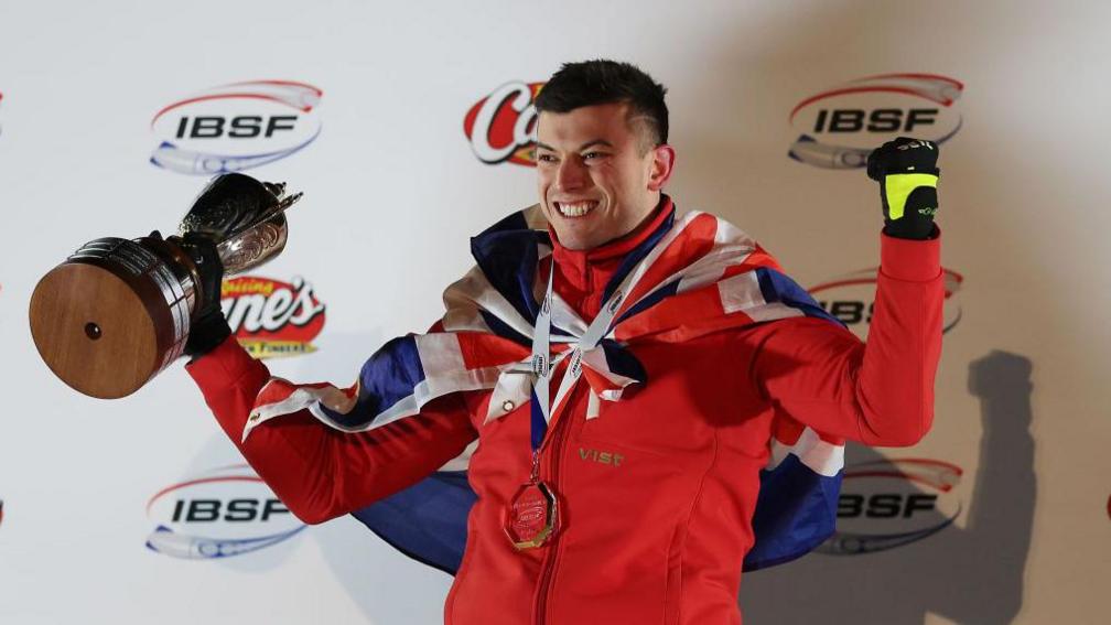 Matt Weston holds the trophy in one hand and clenches his fist in the other after winning the world title