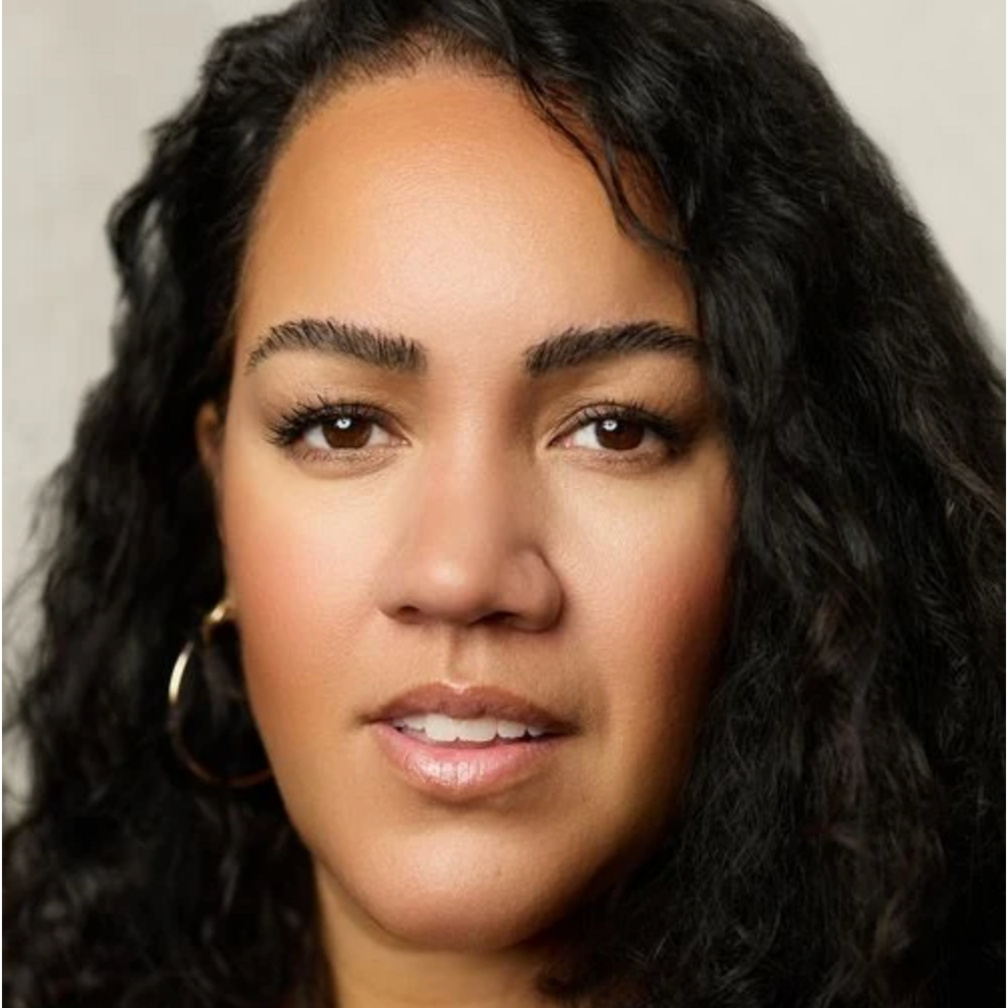 A headshot of Sharon Wattis, a woman with long dark curly hair.