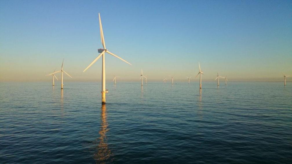 Wind turbines at Sheringham Shoal rising out of the water against a hazy blue sky