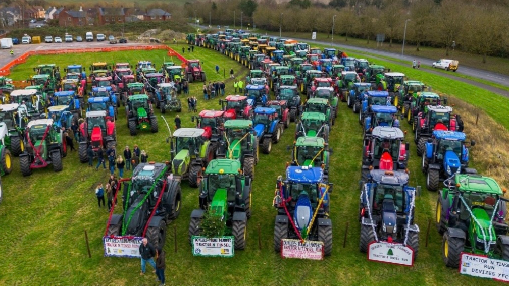 Around 150 tractors, decorated in tinsel and lined up in half a dozen neat rows on a field next to a road, ready to parade