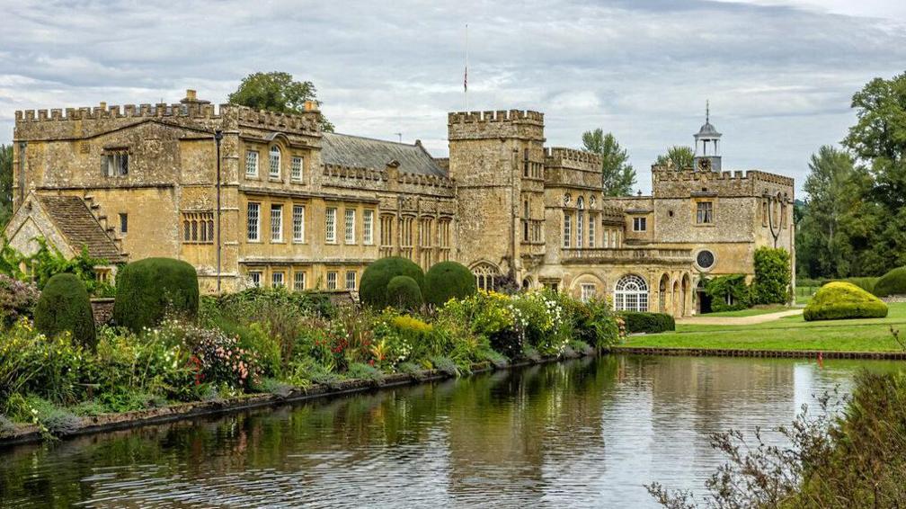 Forde Abbey - a grand historical building topped with crenellations surrounded by gardens. In the foreground is a large rectangular pond.