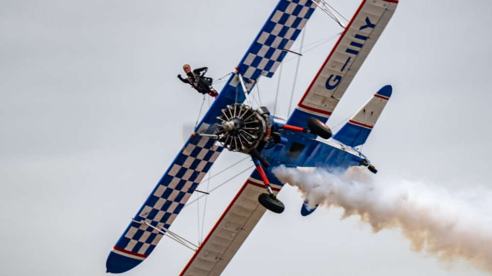A by-plane shown at an angle with a single wing walker at the top