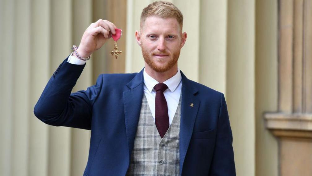 Ben Stokes in a suit with his OBE medal at Buckingham Palace.