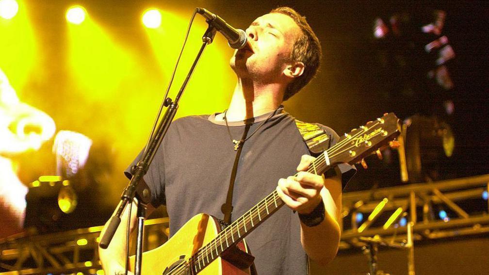 Chris Martin of Coldplay performing on stage with an acoustic guitar in 2000