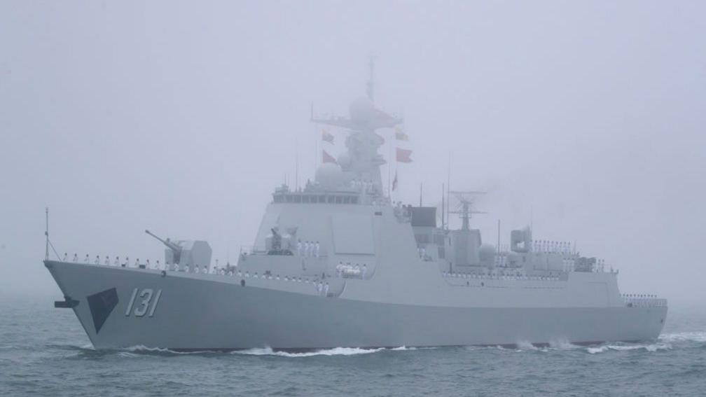 A large navy ship flying Chinese flags sails on misty ocean