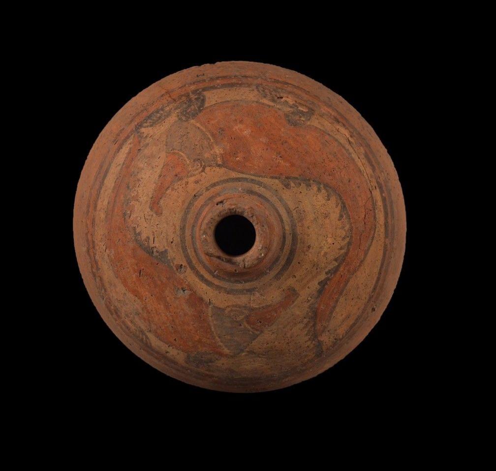 A reddish-brown clay jar on a black background. The jar is decorated with painted crocodiles