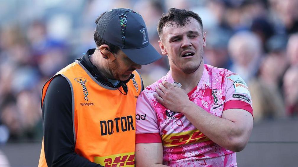 Jarrod Evans (right) walks off the pitch touching his right shoulder as a team doctor stands next to him