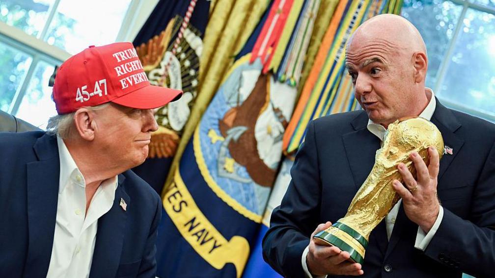 Us president Donald Trump smiles while looking at the Fifa World Cup trophy being held aloft by Fifa president Gianni Infantino in the White House's Oval Office
