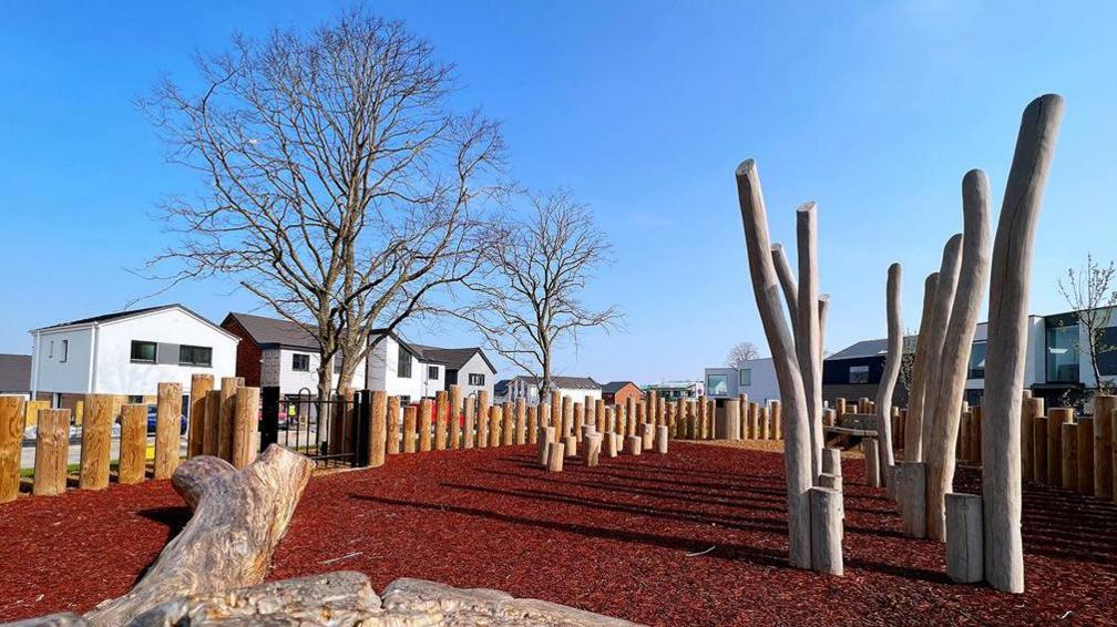 A playground at Graven Hill. It looks like rubber mulch on the ground, with tree branches and logs to play on.