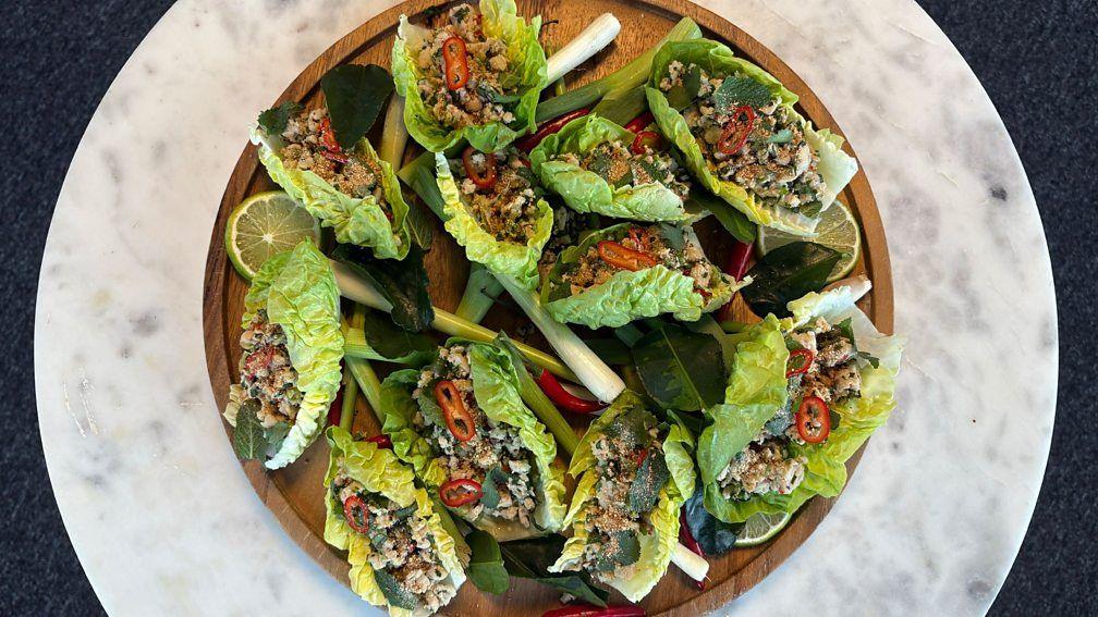 Green salad with lime garnish and minced chicken nested within each lettuce leaf