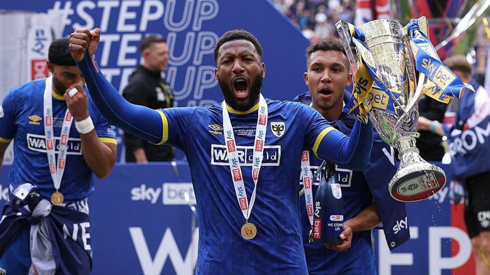 Myles Hippolyte celebrates with the League Two play-off trophy