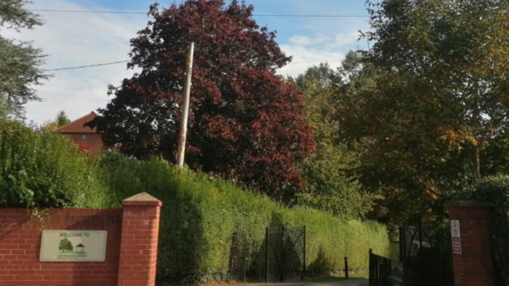 The current entrance to the Lake Pleasure Grounds in Warminster which features a plain brick wall and a sign which says 'Welcome To' with 'Lake Pleasure Grounds' in small text.