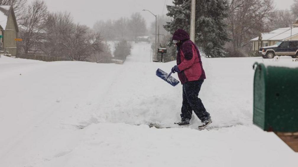 A woman shovels snow from her drive.