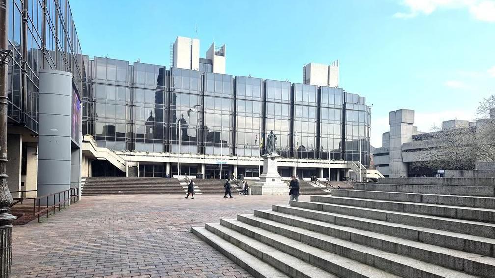 The outside of Portsmouth City Council offices, a concrete building with lots of windows. There is a statue outside the building and concrete steps.