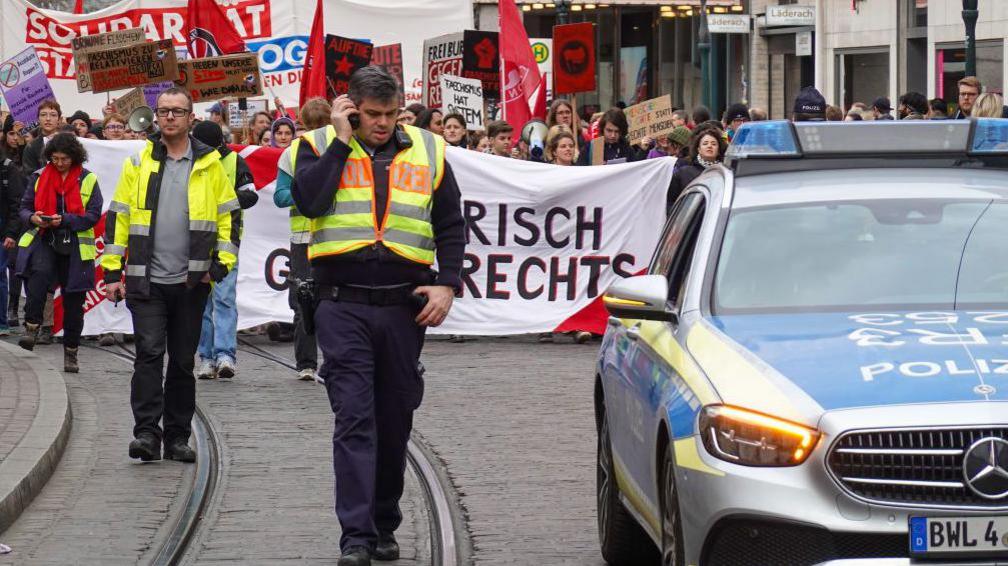 Demonstrators march on a street escorted by German police 