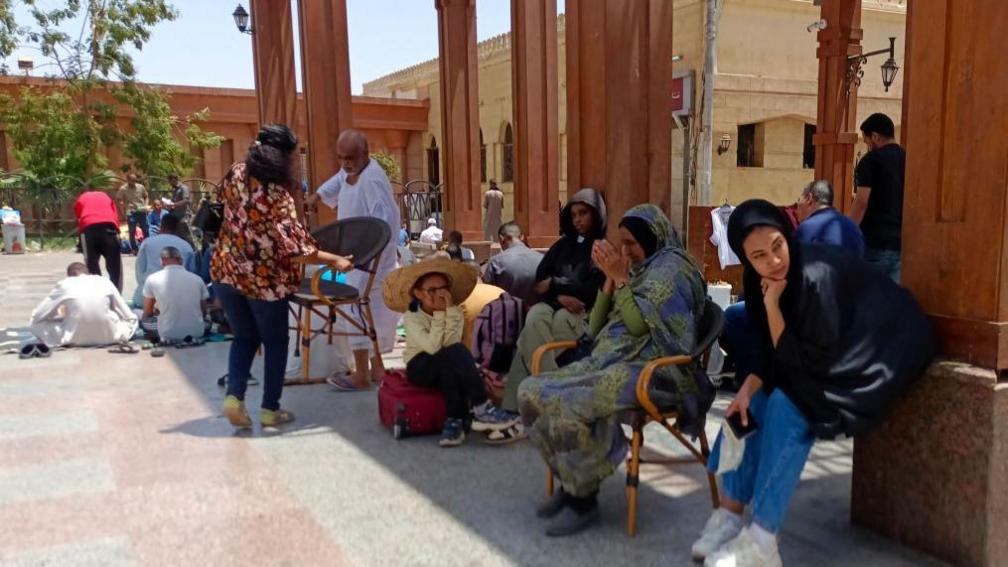 People from Sudan sit down outside a railway station in the Egyptian city of Aswan on 28 April 2023. None of the people pictured are in the article