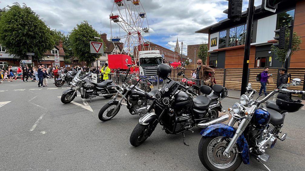 A row of motorbikes parked in front of a McDonald's branch on the right and a ferris wheel in the background.