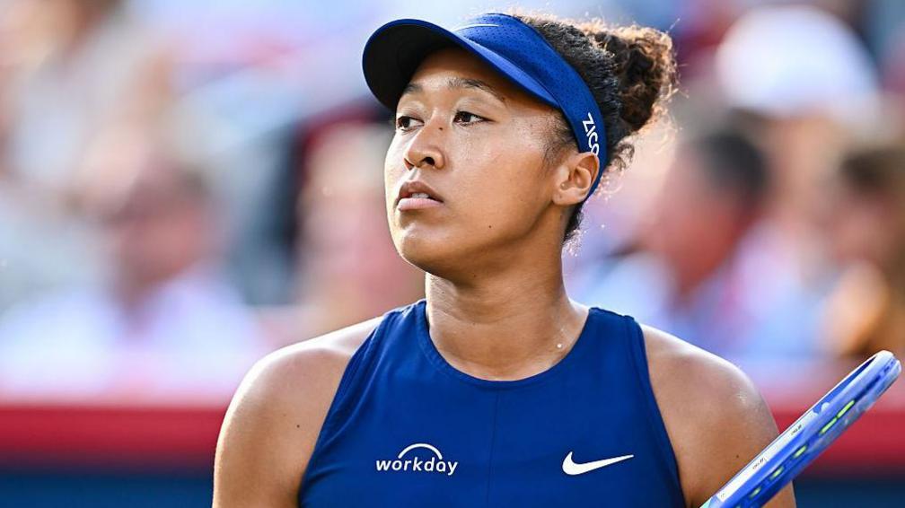 Naomi Osaka wearing a blue hat and a blue vest