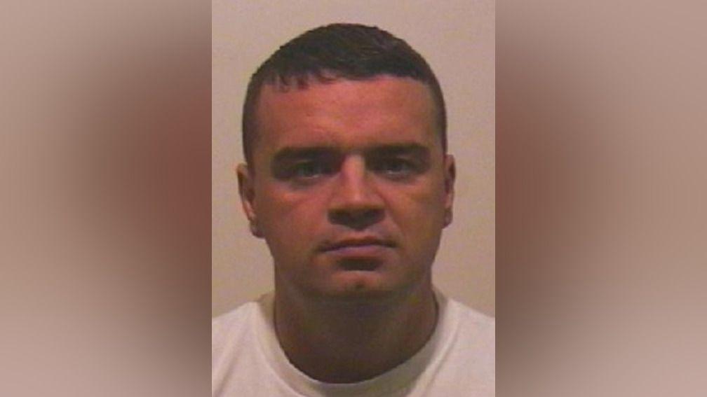Mugshot of Monaghan. He is clean shaven with short dark hair and wears a white t-shirt.