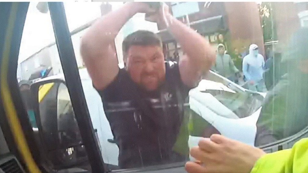 Luke Moran has his hands raised in the air before he punches the driver's seat window of a police van. An officer's hand is seen inside the window, showing that someone was sitting in the driver's seat