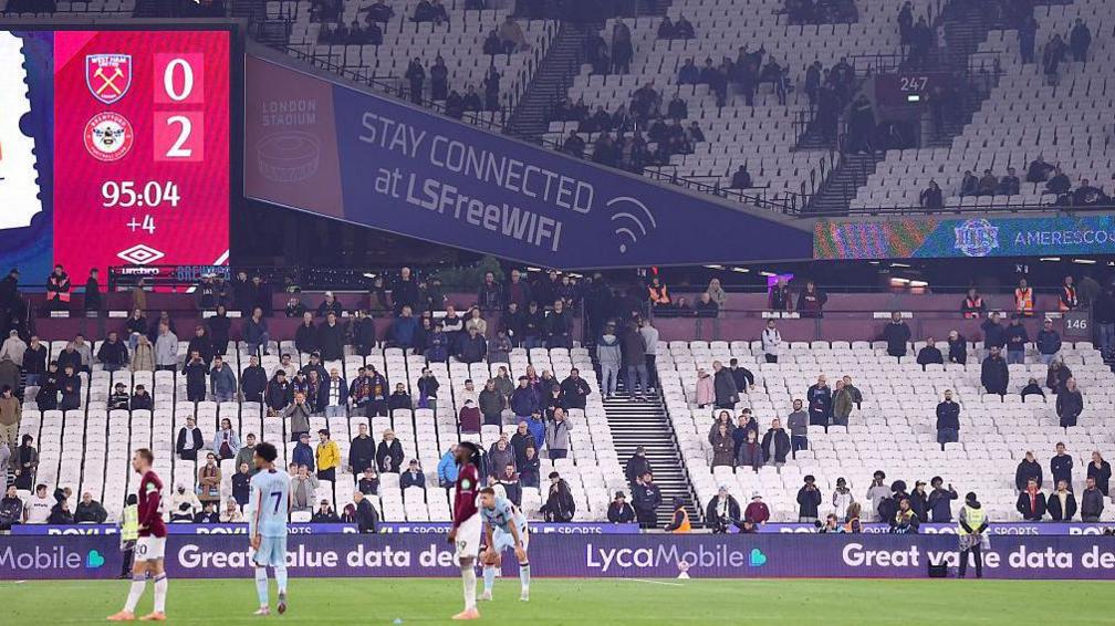 Empty seats in the background as West Ham and Brentford players stand on the pitch
