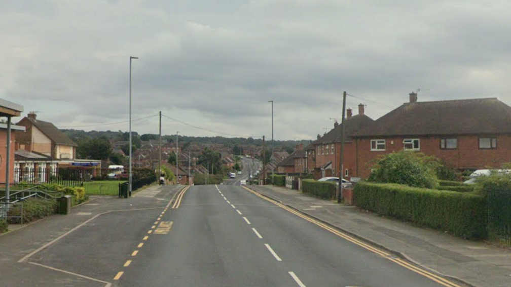 A single carriageway road stretches into the distance. There are houses and buildings on either side