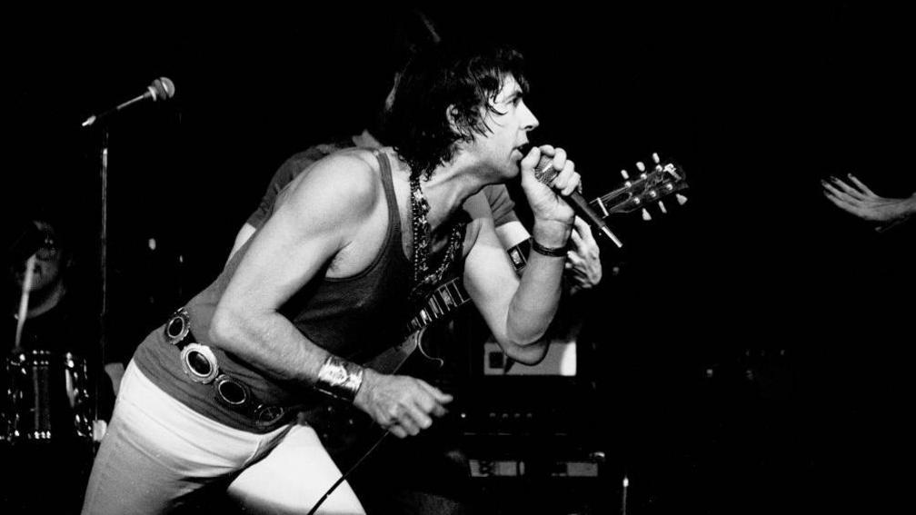 English Blues and Rock musician John Mayall performs onstage at Greenwich Village's Bottom Line nightclub, New York, New York, January 23, 1979. Mostly obscured in the background are Ruben Alvarez, on drums, and Harvey Mandel, on guitar. 