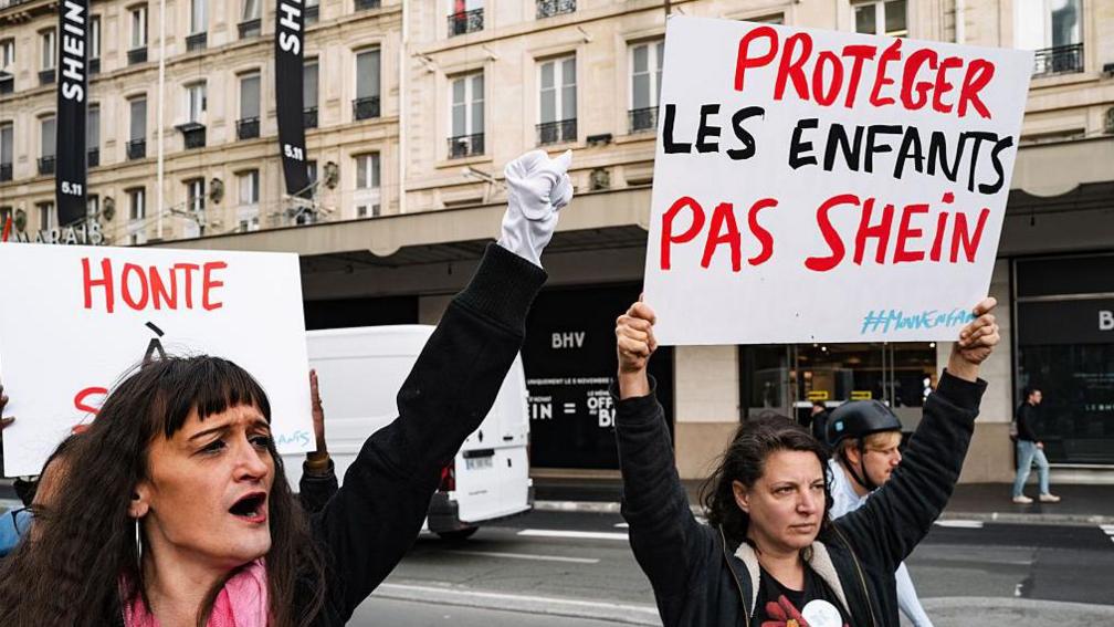 A woman holds a placard that reads ''Protect children, not Shein'' as people protest in front of the BHV department store in Paris, France, on November 5, 2025, on the opening day of Asian e-commerce giant Shein's first physical store at the Bazar de l'Hotel de Ville (BHV) department store