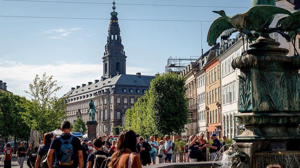 Shoppers and tourists mill about next to a fountain in the pedestrianized Stroget shopping street in Copenhagen, Denmark