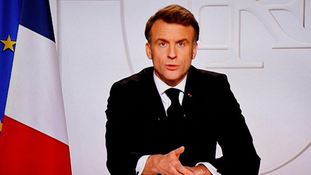 A television screen broadcasting France's President Emmanuel Macron addressing a live interview on French TV.