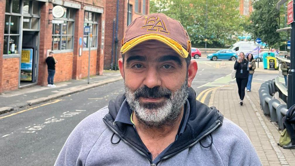 Taxi driver Adel wearing a brown and yellow cap, and grey hoodie.