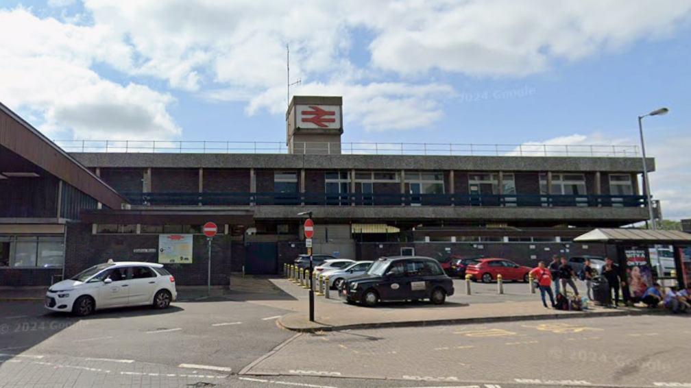 A two storey building with cars and taxis in front. There is a red railway sign on the top of the building