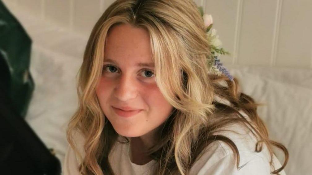 Chloe pictured wearing white t-shirt, and has a bow in her blonde hair. She is smiling at the camera