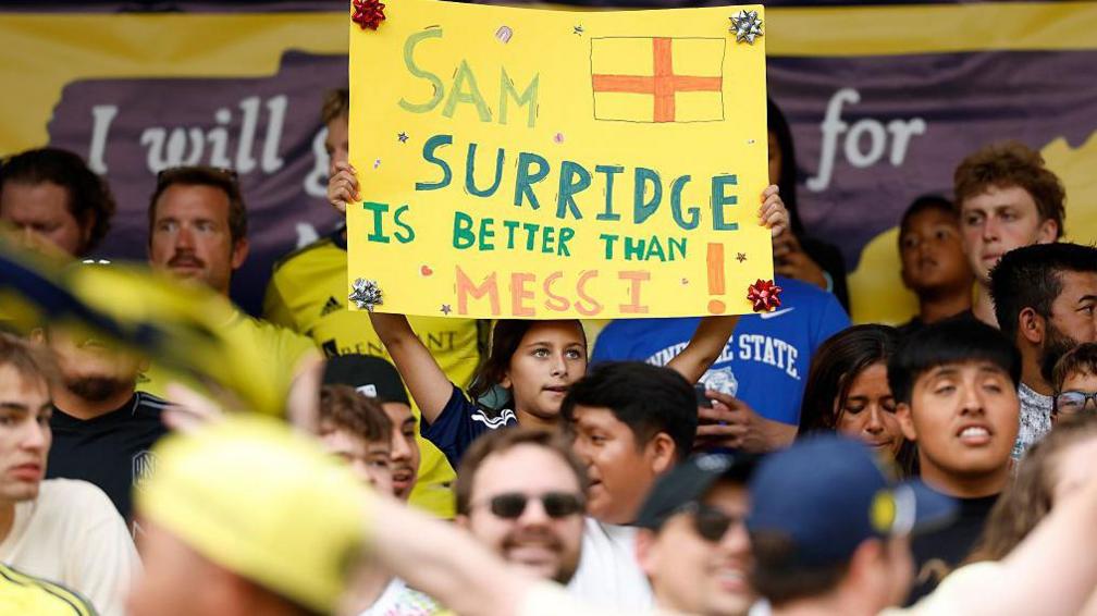 A fan holds up a sign saying "Sam Surridge is better than Messi"