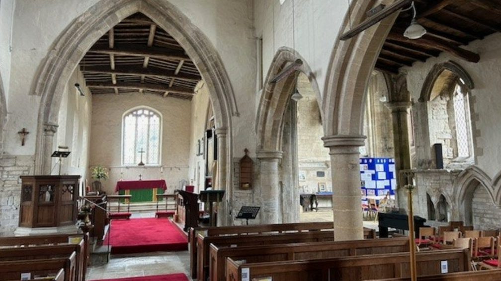 Inside St Andrew's Church are rows of wooden pews, stone arches and a wooden roof. There is a red carpet in front of the altar and in the aisle