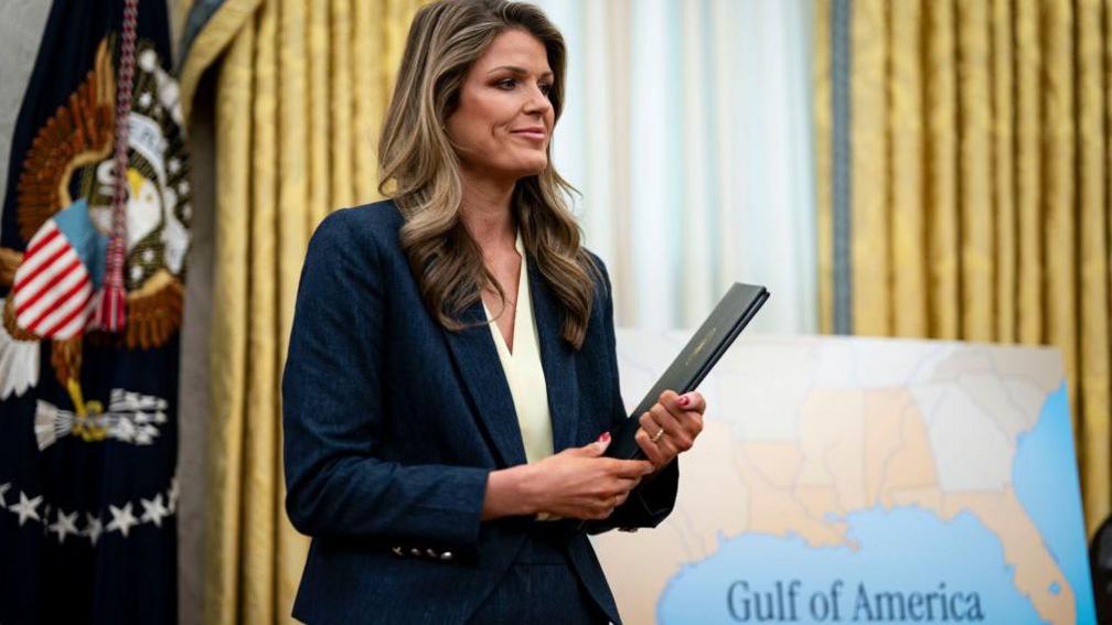 Lindsey Halligan holding a file with the USA flag in the background