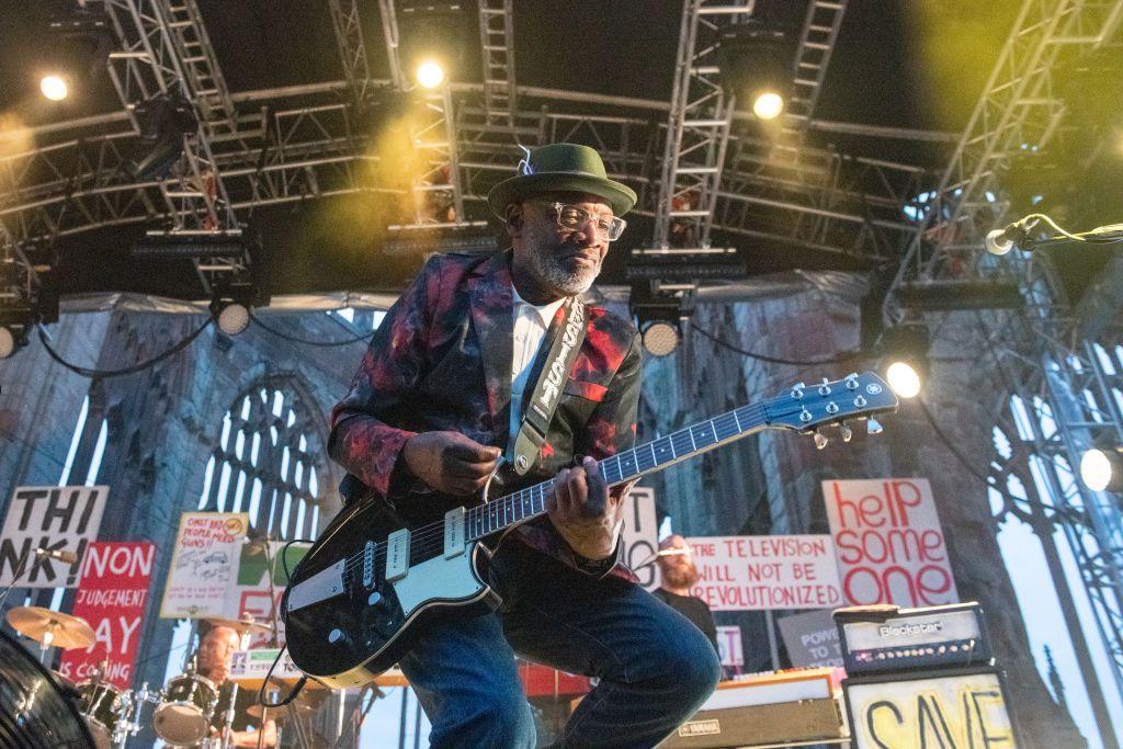 Lynval Golding seen wearing a hat and red jacket playing a guitar during a gig in 2019 with The Specials in the ruins of Coventry Cathedral. 