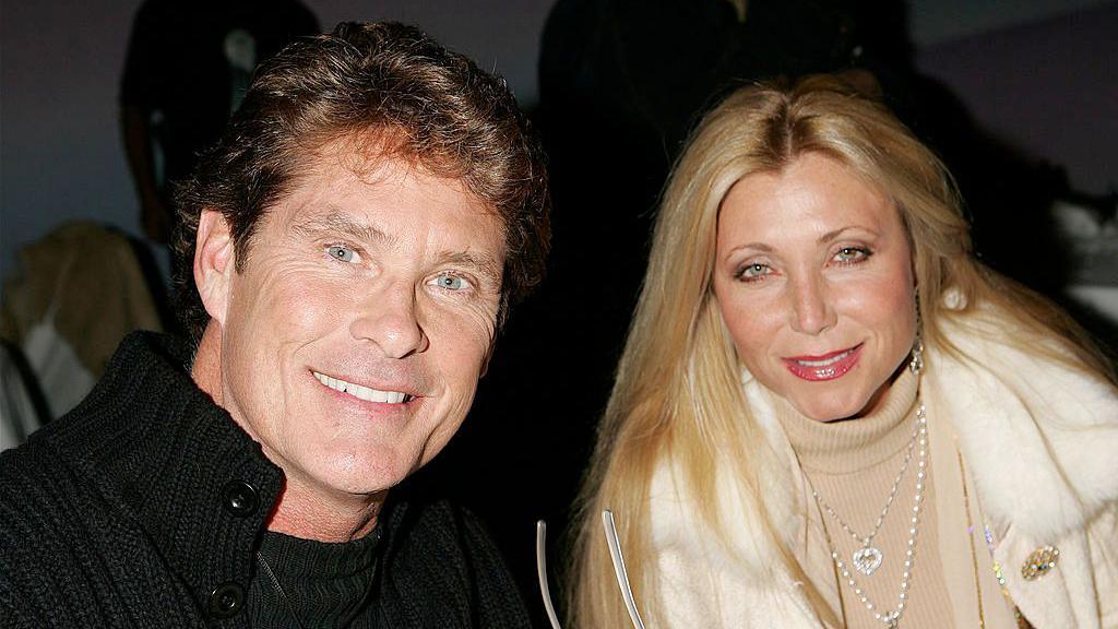 Hasselhoff and Bach seen seated beside each other in 2005. He wears a black sweater and she has long blonde hair, is wearing sparkly jewelry and a white coat.