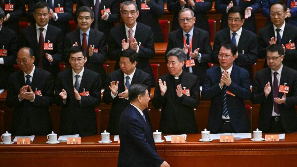 China's President Xi Jinping, in a black suit, walks past other party leaders who are standing and clapping as he arrives for the opening ceremony of the Chinese People's Political Consultative Conference (CPPCC) at the Great Hall of the People in Beijing on March 4, 2025. 