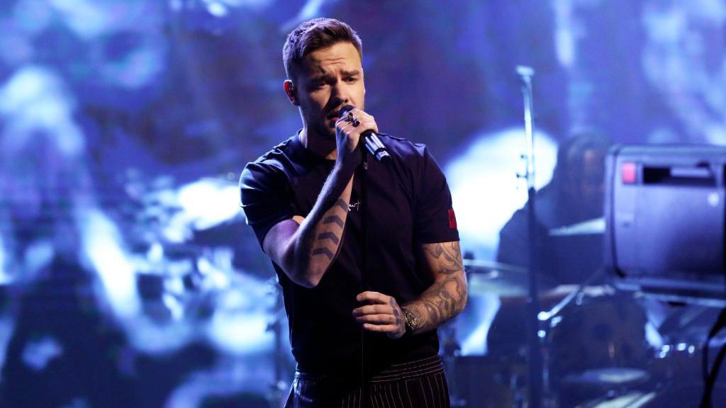 Liam Payne wearing a black T-shirt and holding a microphone while performing songs from his debut solo album on The Tonight Show in 2019