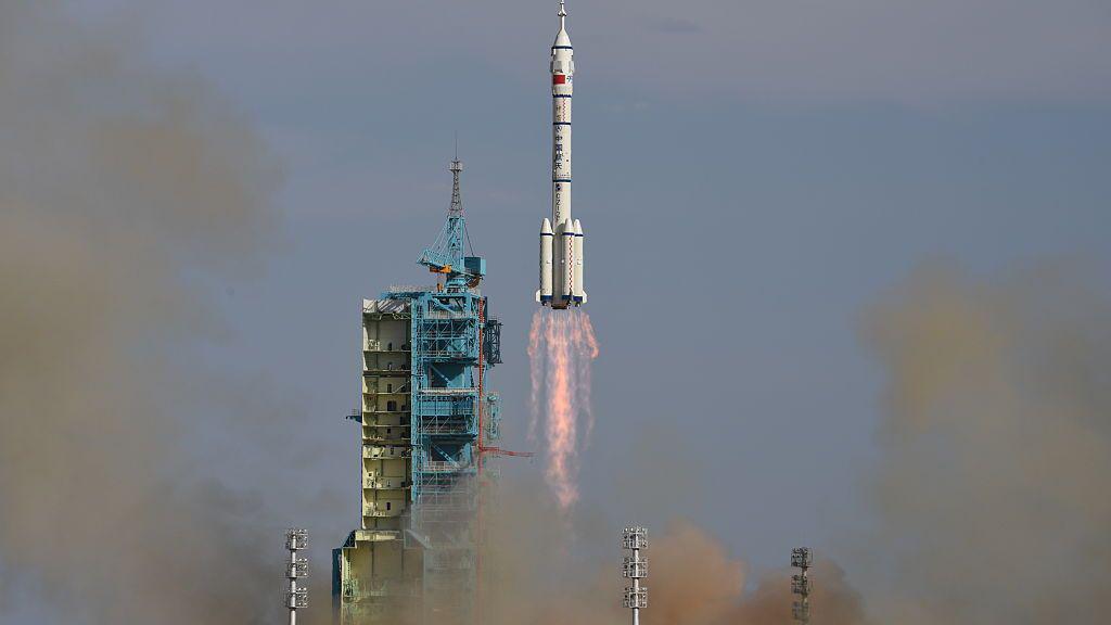 A white rocket launches into space with a red blast below it next to a teal tower.