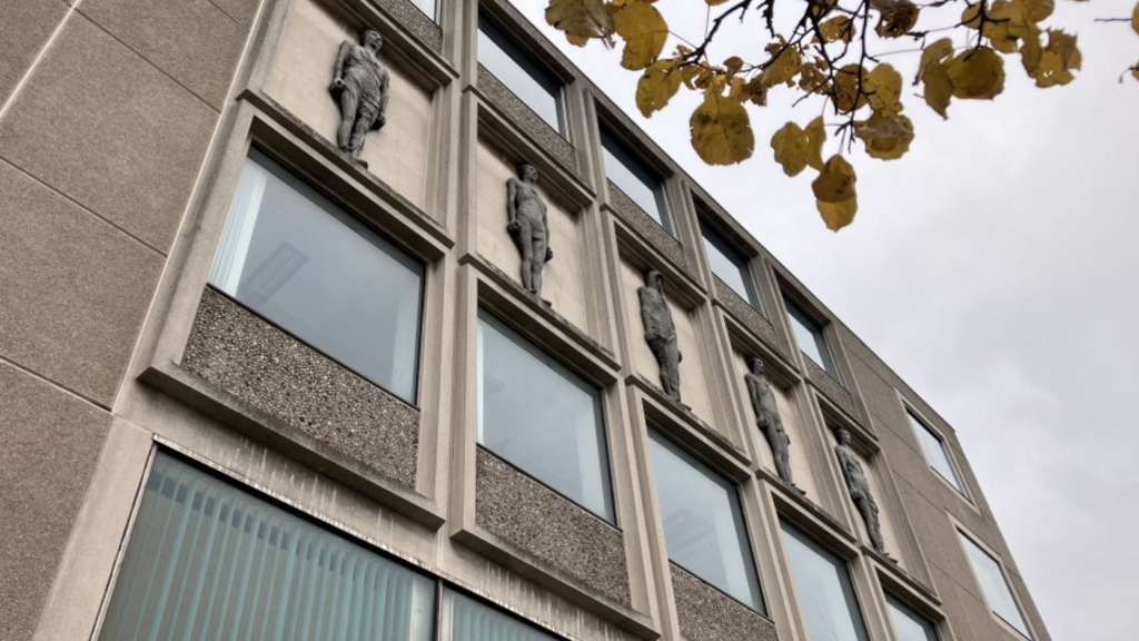 An imposing grey library building with friezes of figures in between rows of windows.